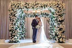 a bride and groom standing in front of an archway decorated with white flowers at their wedding