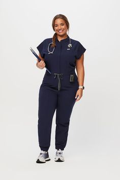 Why We Love ThisCasual and convenient. The FIONx Rafaela ScrubJumpsuit™ features nine pockets, a high rise waistband and gathered elastic cuffs for the best all-in-one option.   Mandarin collar with hidden center front zipper closure 'Weve got you covered' quote on inside placket   Total of nine pockets  Two chest pockets  Two hand pockets  Two drop zipper pockets at waist  Two back drop pockets  One pen sleeve pocket Mandarin collar with hidden center front zipper closure  High rise waistband w Navy Scrubs, Vest Layering, Cargo Jumpsuit, Scrubs Outfit, Navy Jumpsuit, Medical Outfit, Figs Scrubs, Back Drop, Womens Scrubs