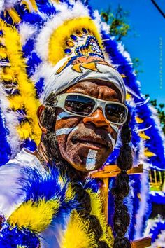 a man with his face painted in blue, yellow and white feathers is standing next to a pole