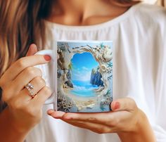 a woman holding a coffee mug with an image of the ocean and rocks on it