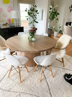 a dining room table with white chairs and a vase filled with flowers on top of it