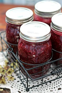 four jars of pickled fruit sit on a wire rack next to a lace doily