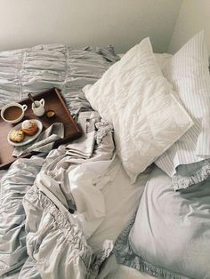 an unmade bed with two cups of coffee and pastries on the tray next to it