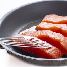 two pieces of salmon in a frying pan with a fork