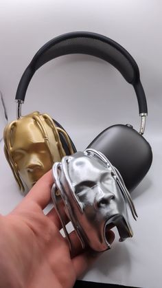 a hand is holding two headphones with different colors and designs on them, while the other one has its mouth open