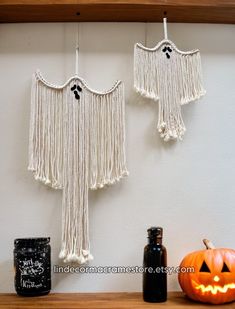 two white macrame tassels hanging from a shelf next to pumpkins