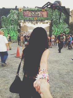 a woman is holding her hand out in front of an entrance to a festival with people walking around