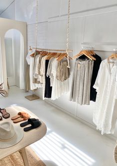 clothes are hanging in a room with white walls and flooring, along with a hat on a table