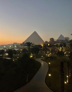 the sun is setting in front of two pyramids at night, and there are lights on either side of the path