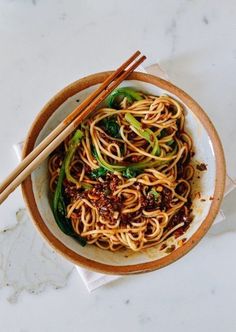 a bowl filled with noodles and vegetables next to chopsticks on a white table