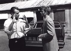 two men standing next to each other in front of a car