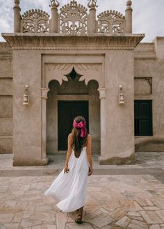 a woman in a white dress is walking towards a building with an ornate archway and doorway