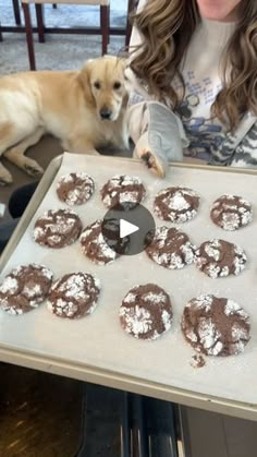 a woman holding a tray with cookies on it and a dog sitting next to her