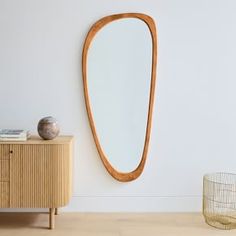 an oval wooden mirror hanging on the wall next to a dresser and sideboard in a white room