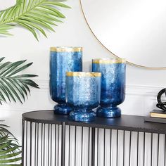 three blue vases sitting on top of a table next to a mirror and plant