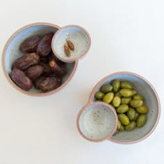 two bowls filled with different types of olives and some nuts on the table top