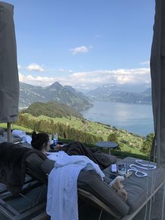 a woman laying on top of a chaise lounge chair next to a lake and mountains