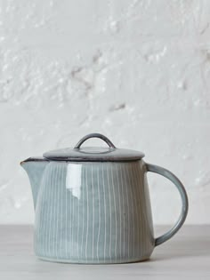 a ceramic tea pot with a handle on a wooden table next to a white wall