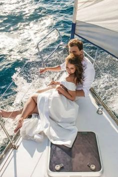 a man and woman sitting on the back of a sailboat in the ocean looking at their cell phones