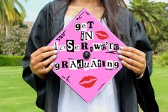 a woman holding a pink graduation cap with words on it