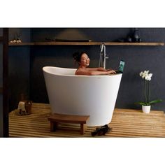 a woman taking a bath in a large white tub next to a shelf with flowers