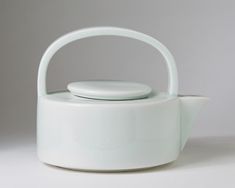 a white tea pot with a lid and handle on the side, against a gray background