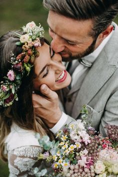 a man in a suit and tie kissing a woman with flowers on her head while she is wearing a flower crown