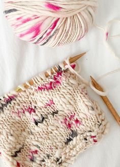 two skeins of yarn and knitting needles on a white surface with pink and black speckles