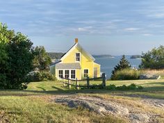 a small yellow house sitting on top of a lush green field next to the ocean