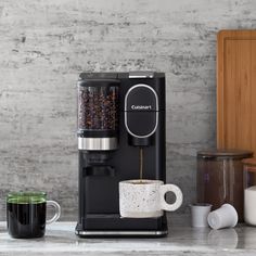 a coffee maker is on the counter next to two cups