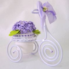 a purple flower arrangement sitting on top of a white cup with spiral handles and flowers in it