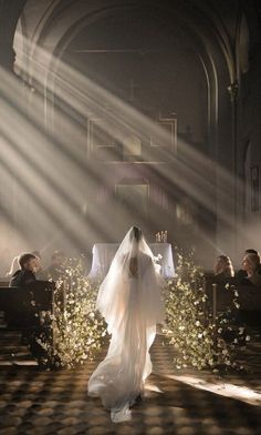 the bride is walking down the aisle with her veil blowing in the wind and sunlight streaming through