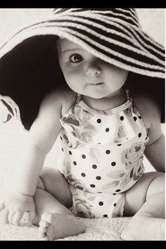 a baby sitting on the ground wearing a hat