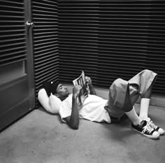 a man laying on the ground reading a book in front of a closed door with shutters