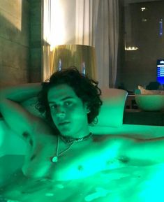 a man laying in a hot tub with green light on his chest and arm around him