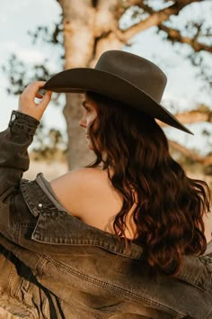 a woman wearing a cowboy hat and jeans looking off into the distance with trees in the background