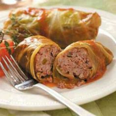 a white plate topped with meat and vegetable rolls next to a fork on top of a table