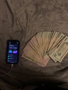 a cell phone sitting on top of a bed next to lots of money in front of it