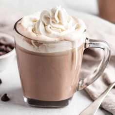 there is a cup of hot chocolate with whipped cream on top and coffee beans in the background