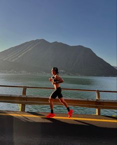 a man running on the side of a road next to a body of water with mountains in the background