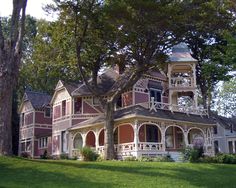 an old victorian style house in the middle of a grassy area with trees and bushes