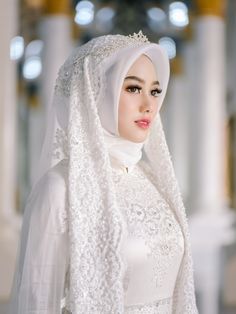 a woman in a white dress with a veil on her head is posing for the camera