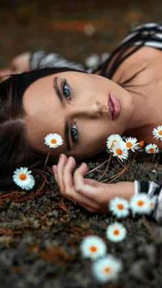 a woman laying on the ground with daisies in her hair and looking at the camera