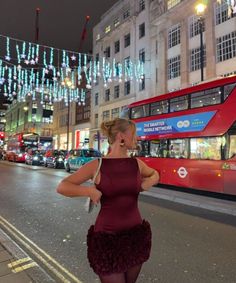 a woman in a short dress is standing on the side of the road near a double decker bus