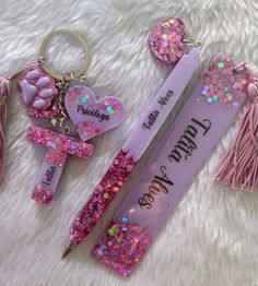 two pens with pink glitters on them next to a keychain and some tassels