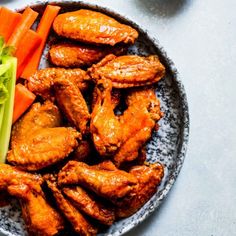 a plate with chicken wings, carrots and celery on it next to other foods