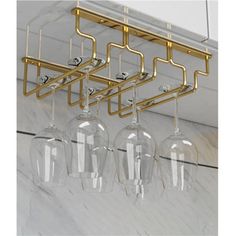 three wine glasses hanging from the ceiling in front of a white marble wall with gold bars