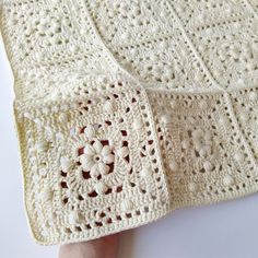 a crocheted blanket is being held up by a person's hand on a white surface