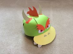 a green paper toy with horns on it's head sitting on the floor in front of a carpet