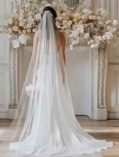 the back of a bride's wedding dress in front of a floral arch with white flowers